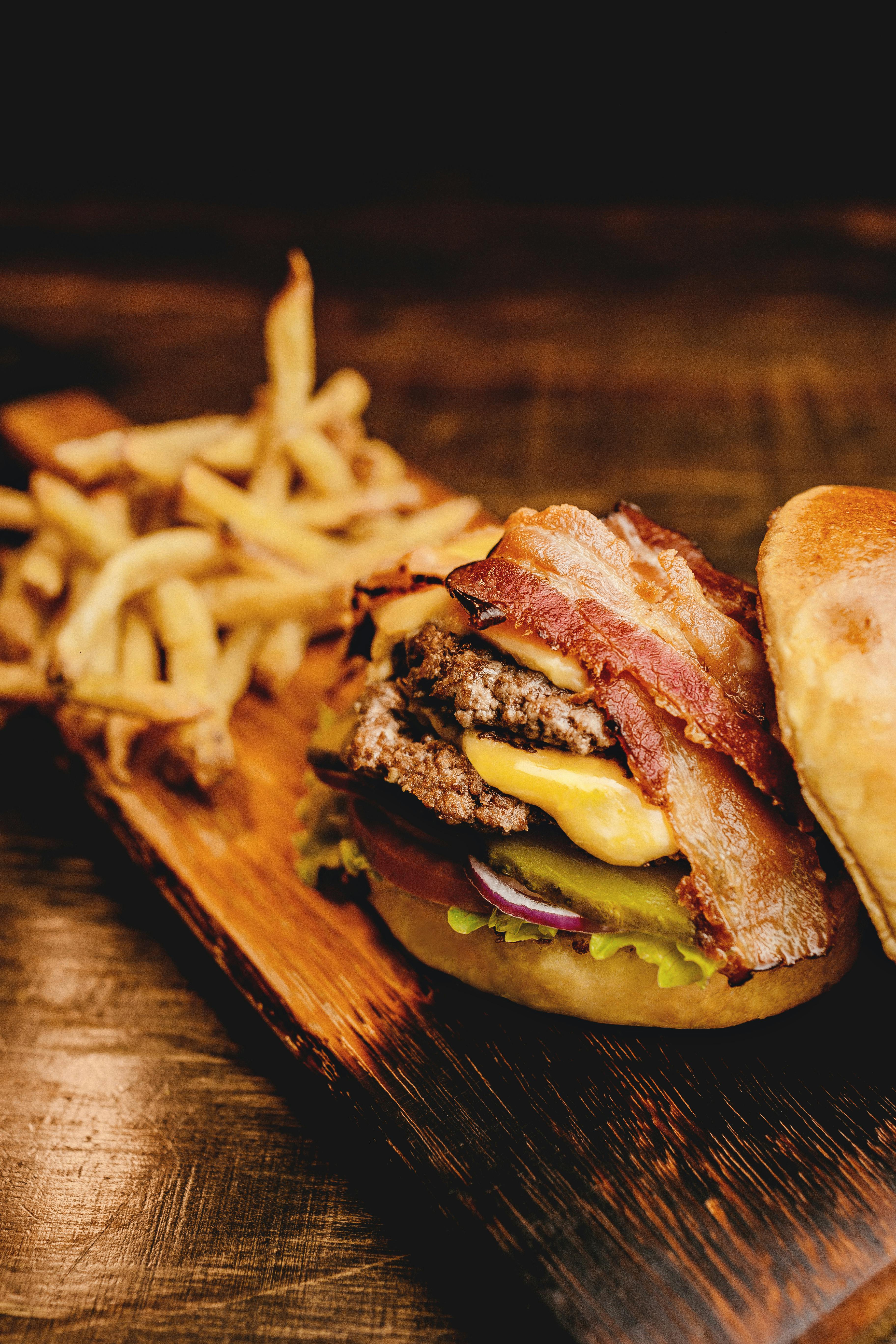 Cheeseburger double avec bacon et frites servi sur une assiette en bois